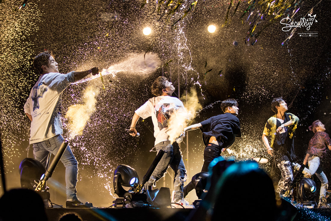 A group of performers on stage celebrating with sprays of confetti and water, creating a dynamic and energetic atmosphere at a concert.