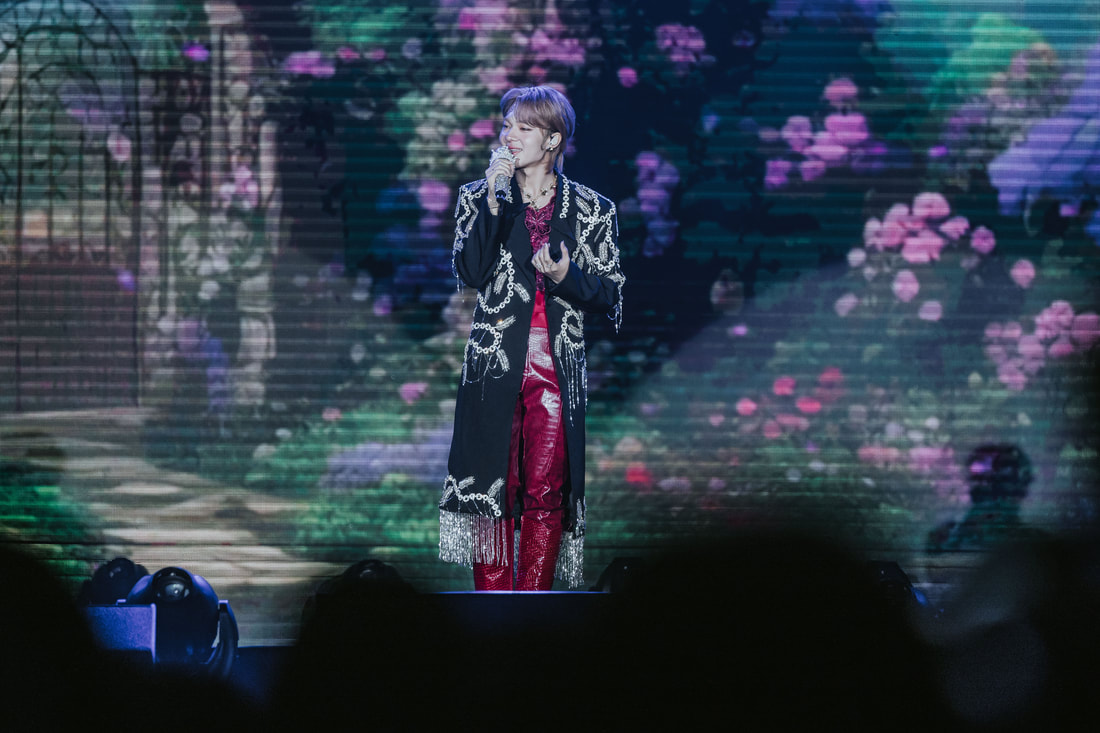 A singer performing on stage in a decorative outfit with a floral background during a live concert.