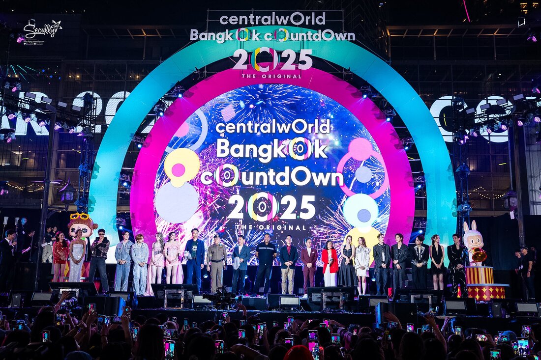 A lively New Year's countdown event at centralWorld in Bangkok, featuring a colorful stage with a vibrant backdrop displaying 'Bangkok Countdown 2025'. A diverse group of performers and guests stands on stage, while a crowd is visible in the foreground, recording the event with their phones.