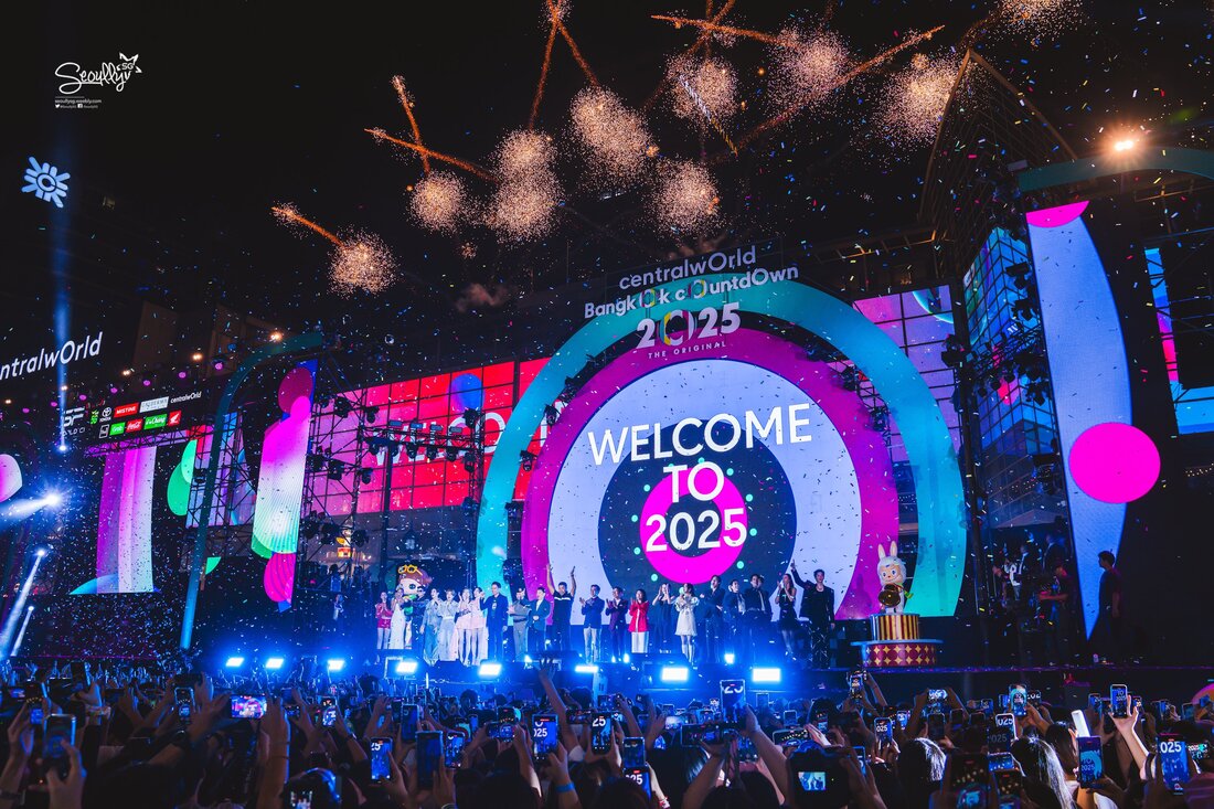 Crowd celebrating at CentralWorld in Bangkok for New Year countdown to 2025, featuring vibrant fireworks and colorful confetti, with a large screen displaying 'Welcome to 2025'.