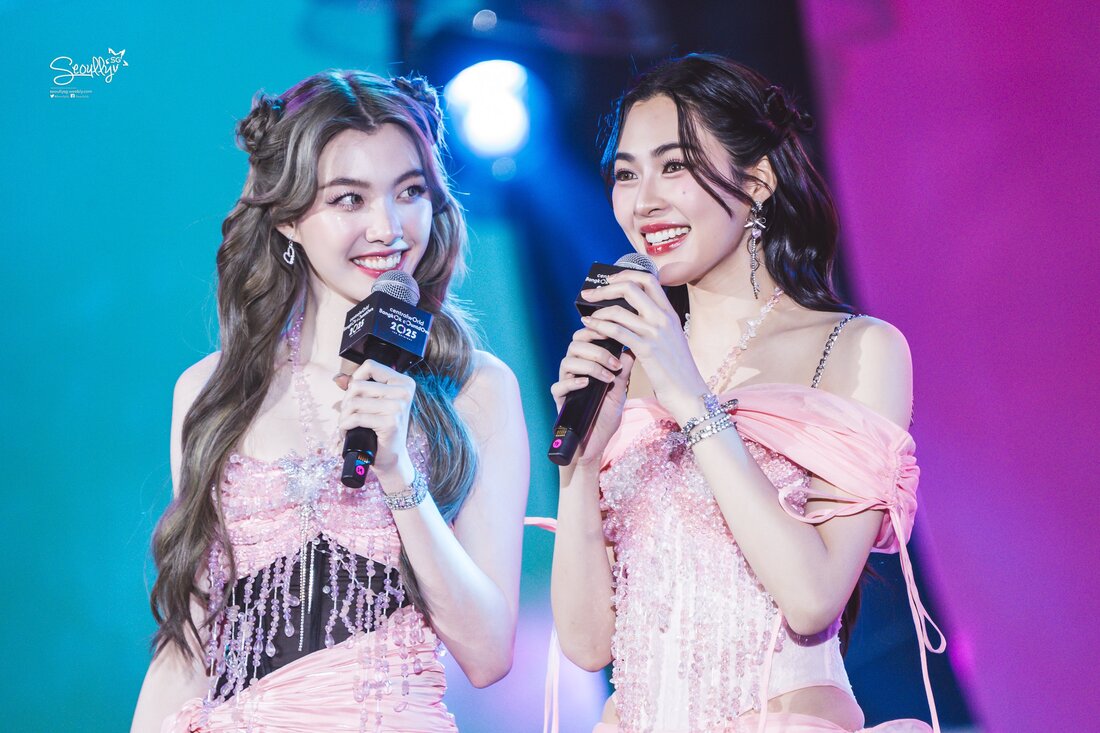 Two women in elegant pink outfits smiling and holding microphones while engaging in conversation on stage.