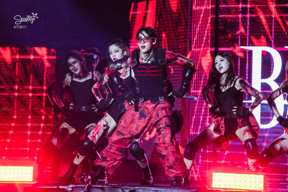 A dynamic performance by female dancers in striking costumes featuring red and black colors, with dramatic makeup and bold poses on stage.