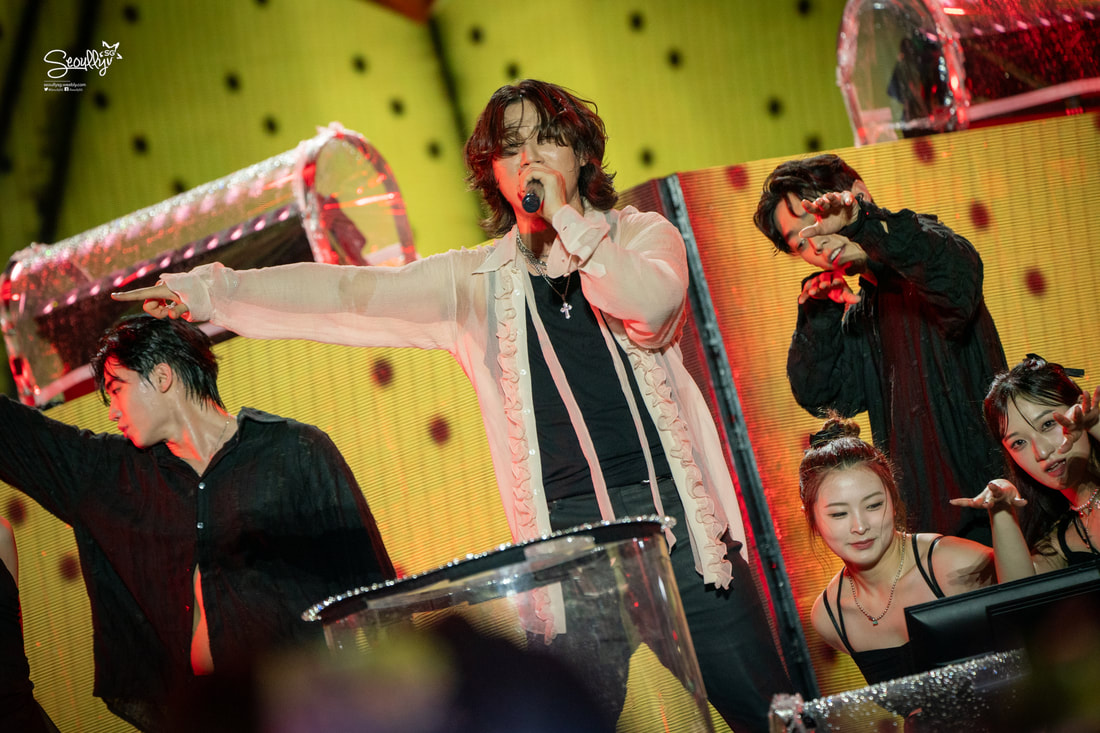 A singer performs on stage with a microphone, surrounded by backup dancers at a lively concert.