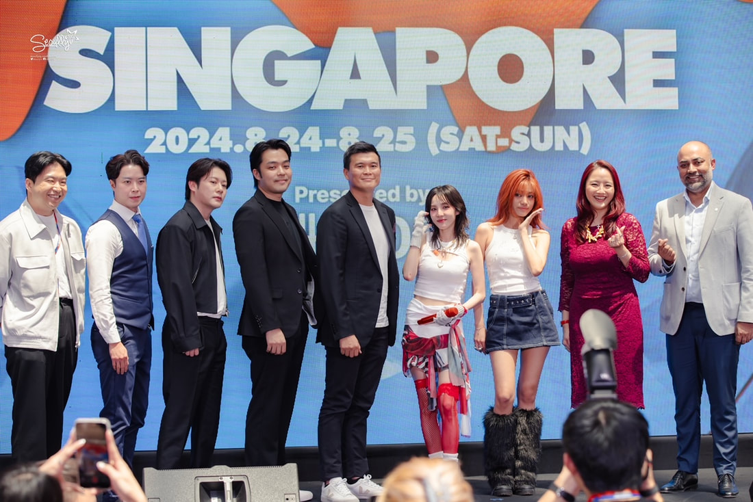 A group of nine individuals posing together on stage in front of a large screen displaying 'SINGAPORE 2024. 8. 24-8. 25 (SAT-SUN)'