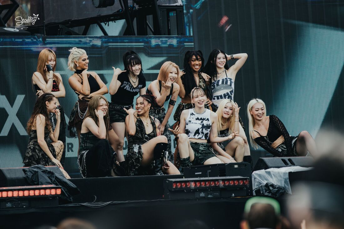 A group of performers in stylish outfits posing on stage, smiling and making playful gestures during a live event.