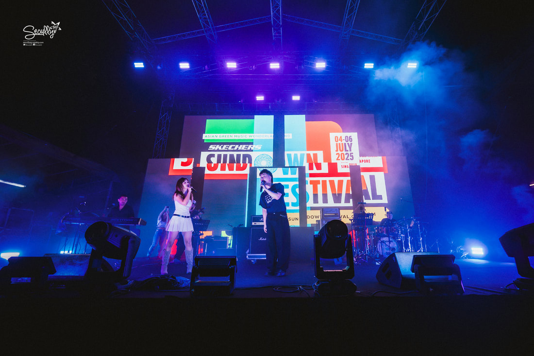 A lively concert scene featuring a male and female performer on stage with vibrant lights and a colorful backdrop, promoting the Sundown Festival taking place in Singapore from July 4-6, 2025.