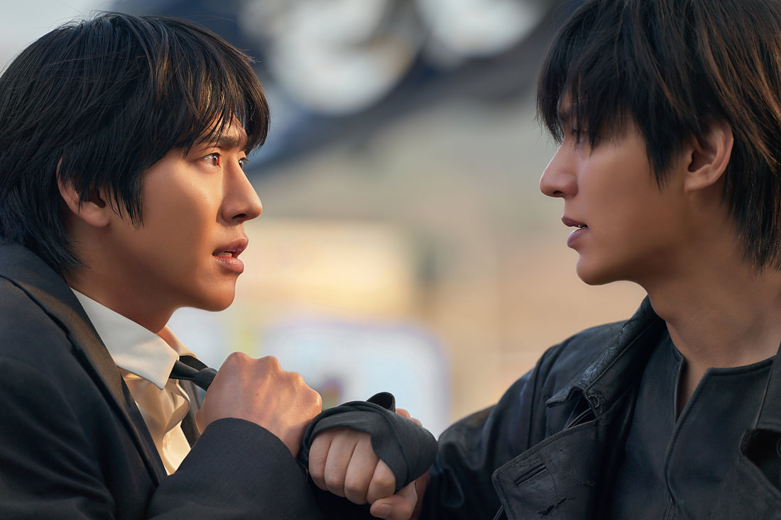Two men face each other in an intense confrontation, one in a suit and the other in a dark jacket, both displaying strong emotions.