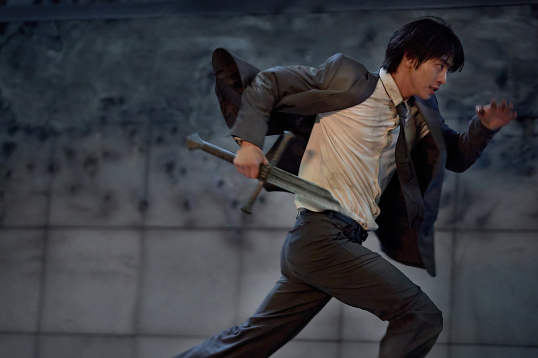 A male figure in a suit running with a sword in hand, showcasing action and urgency against a blurred background.