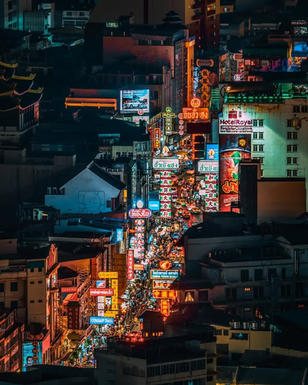 A vibrant city street at night filled with colorful neon lights and bustling crowds, showcasing various signs and storefronts.
