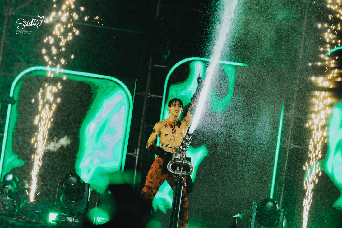 A performer on stage using a water cannon, with streams of water and sparks shooting out, surrounded by vibrant green lighting.