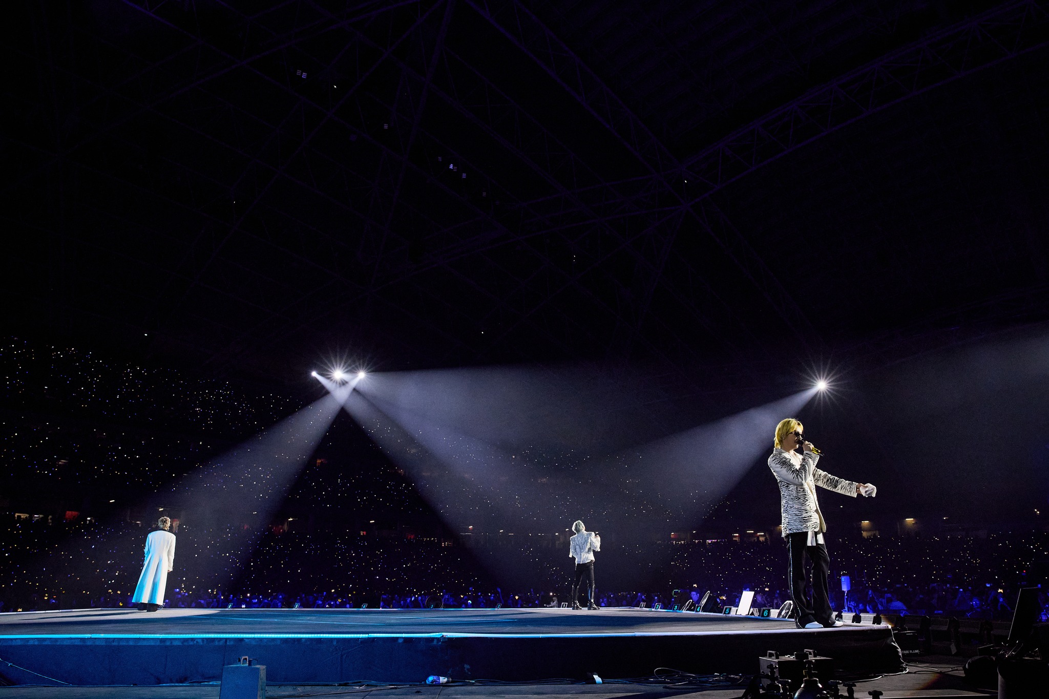 A live concert scene featuring performers on stage with dramatic lighting and an enthusiastic crowd in a large arena.