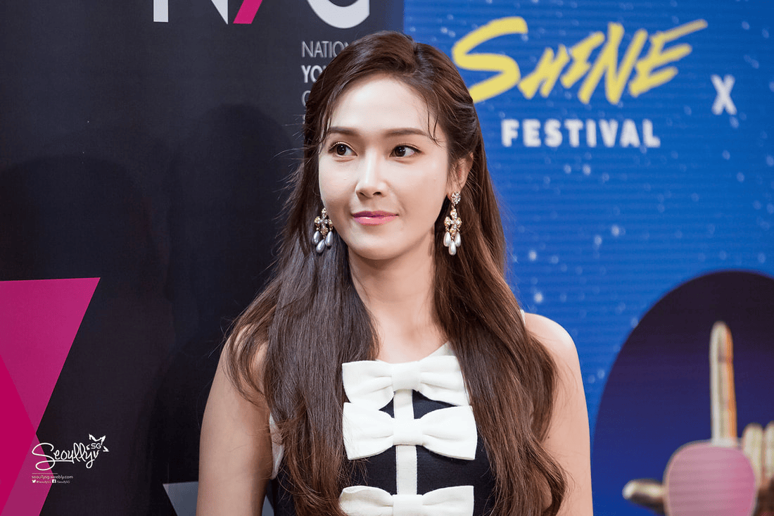 A woman with long hair wearing a black and white dress with a large bow, standing in front of a colorful backdrop featuring event branding.