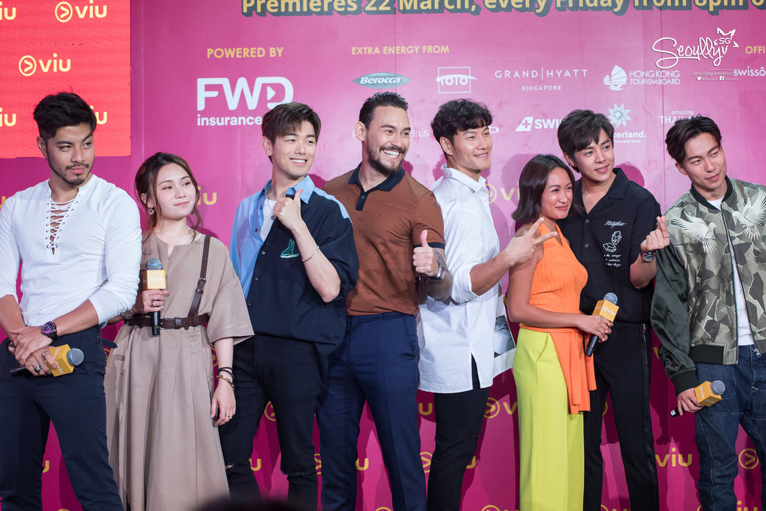 Group of seven individuals posing confidently at a promotional event, each dressed in stylish clothing, with a vibrant pink background featuring the Viu logo.